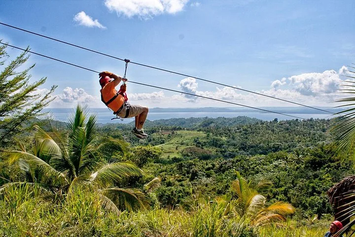 Person ziplining with a scenic view of the ocean and hills.