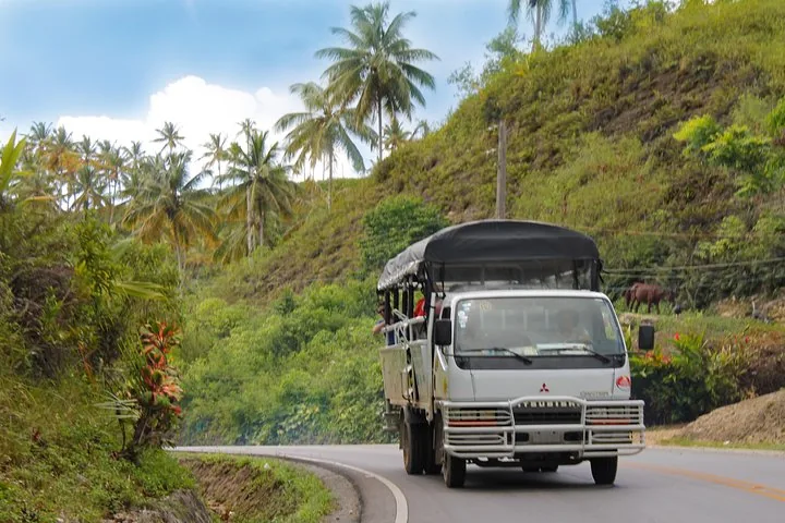 Camion safari che percorre una strada circondata da colline tropicali.