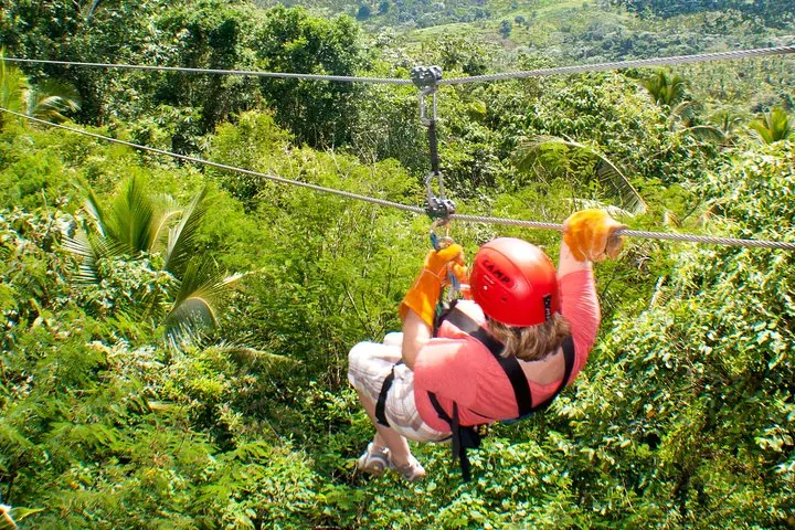 Person beim Ziplining rückwärts über einem dichten, grünen Tropenwald.